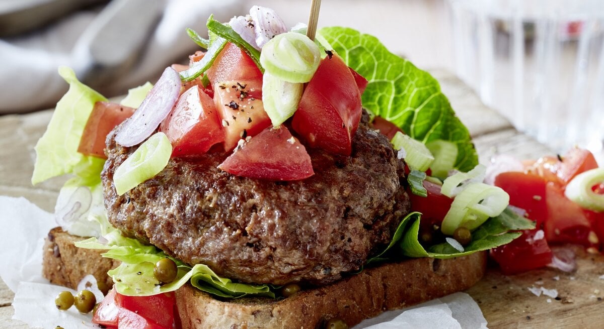Leichter Beef-Burger mit grünem Pfeffer auf Holzunterlage, im Hintergrund Geschirr.