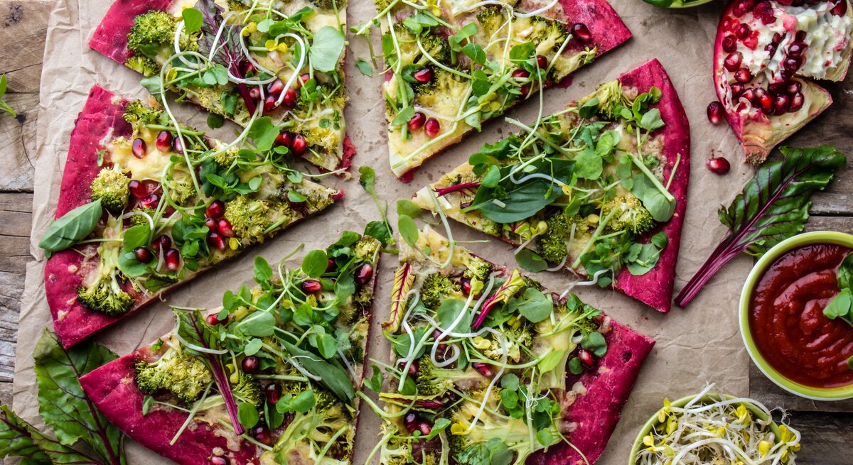 Eine in Stücke geschnittene Rotkohl-Pizza mit Salat, Sprossen und Granatapfelkernen in der Draufsicht.