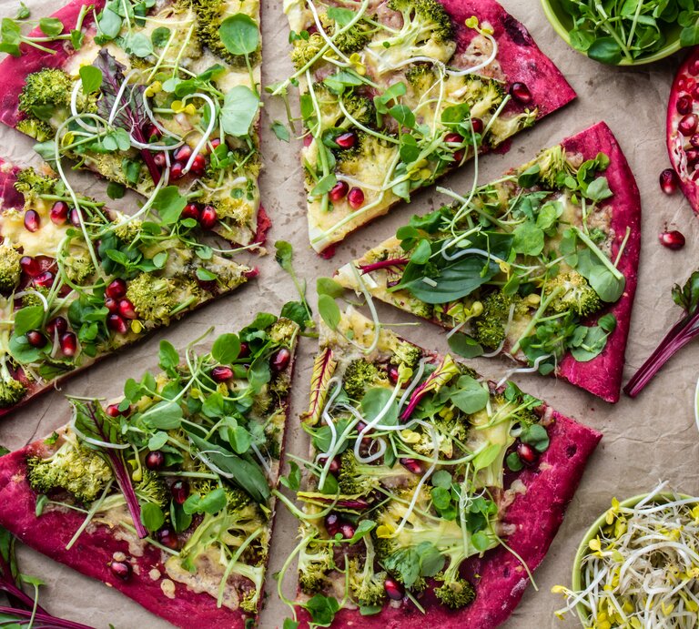 Eine in Stücke geschnittene Rotkohl-Pizza mit Salat, Sprossen und Granatapfelkernen in der Draufsicht. | © Shutterstock/ Larisa Blinova