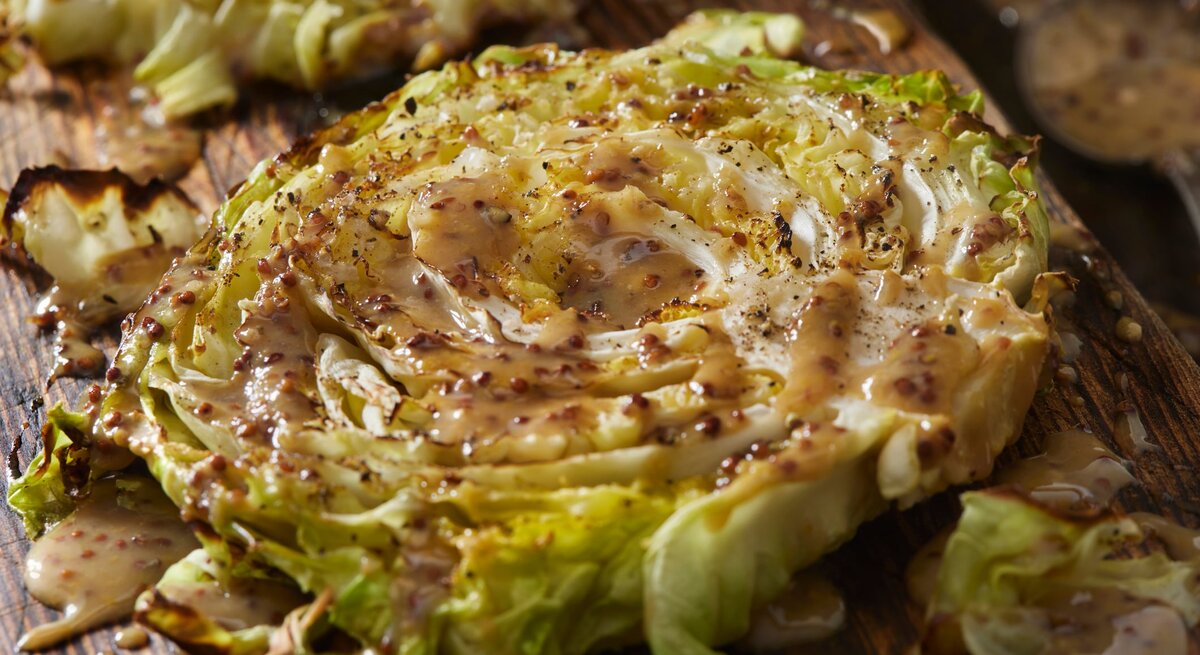 Gebackene Kohl-Steaks an Senf-Soße auf Holzbrett.