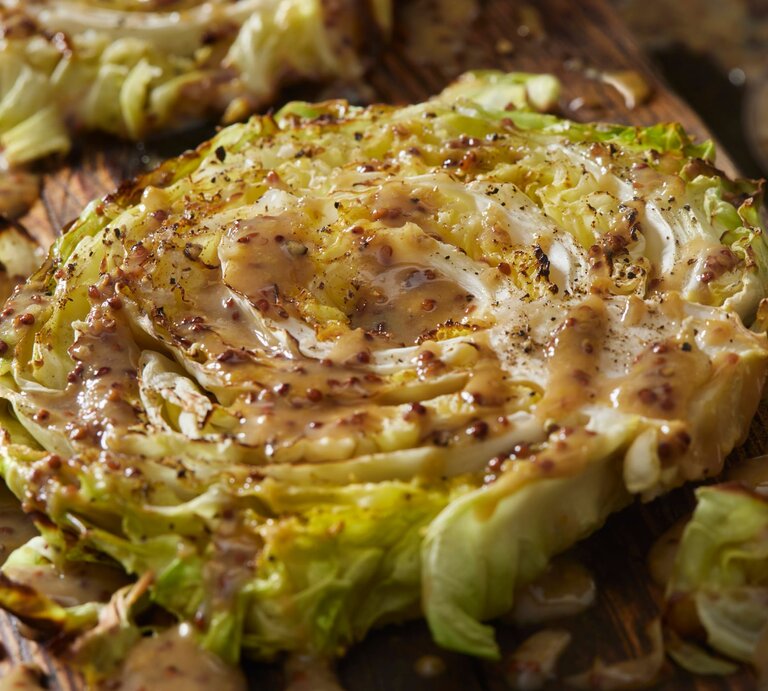 Gebackene Kohl-Steaks an Senf-Soße auf Holzbrett. | © Getty Images/LauriPatterson