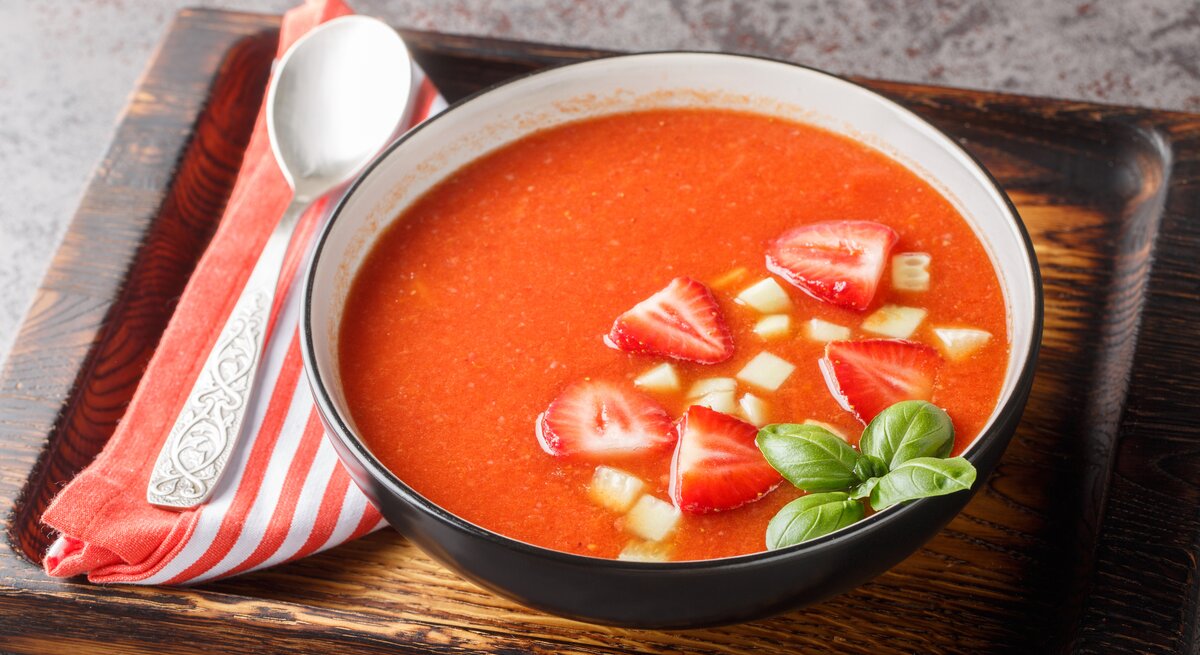 Tomaten-Erdbeer-Gazpacho in Schwarzer Suppenschüssel auf Holzbrett.