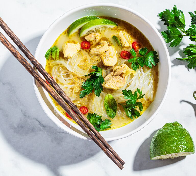 Eine weiße Schüssel mit Thai-Currysuppe mit Nudeln auf einem weißen Tisch. | © AdobeStock/vaaseenaa