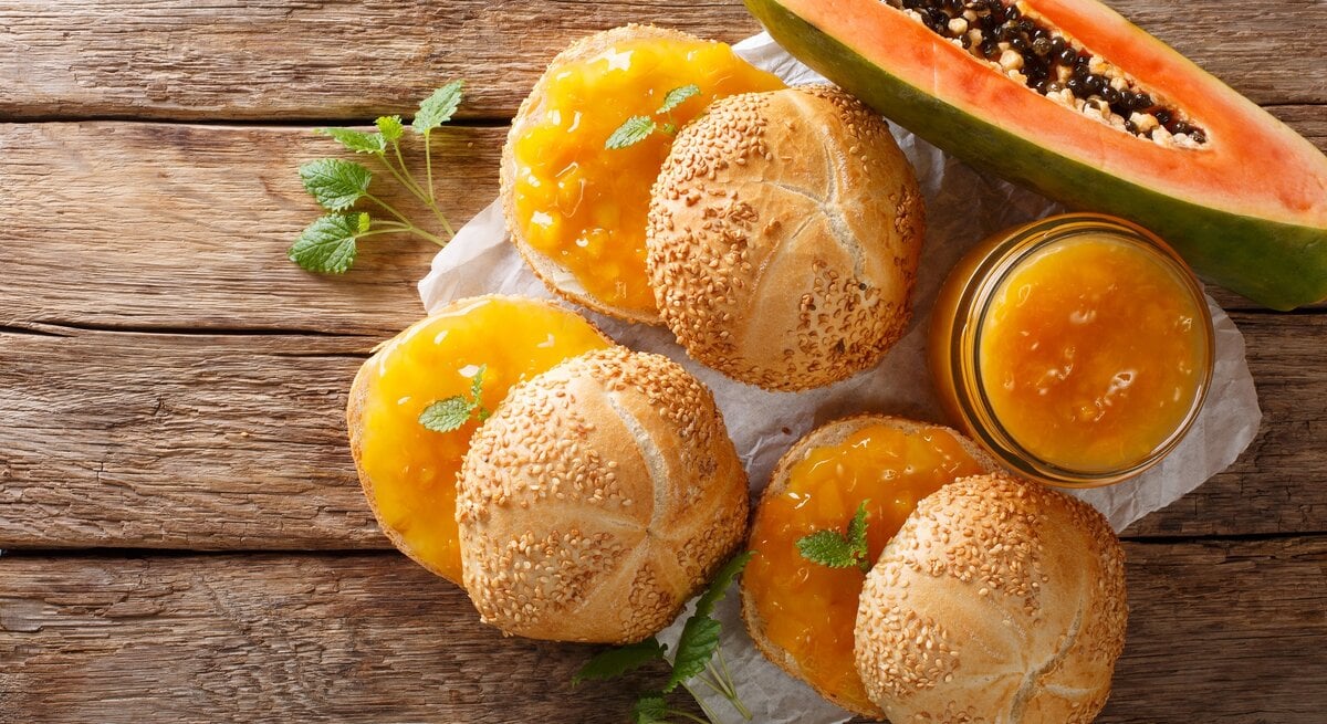 Draufsicht: Drei Brötchen mit einem selbst gemachten Papaya-Aufstrich auf einem Untergrund aus Holz. Daneben liegt eine aufgeschnitten Frucht.
