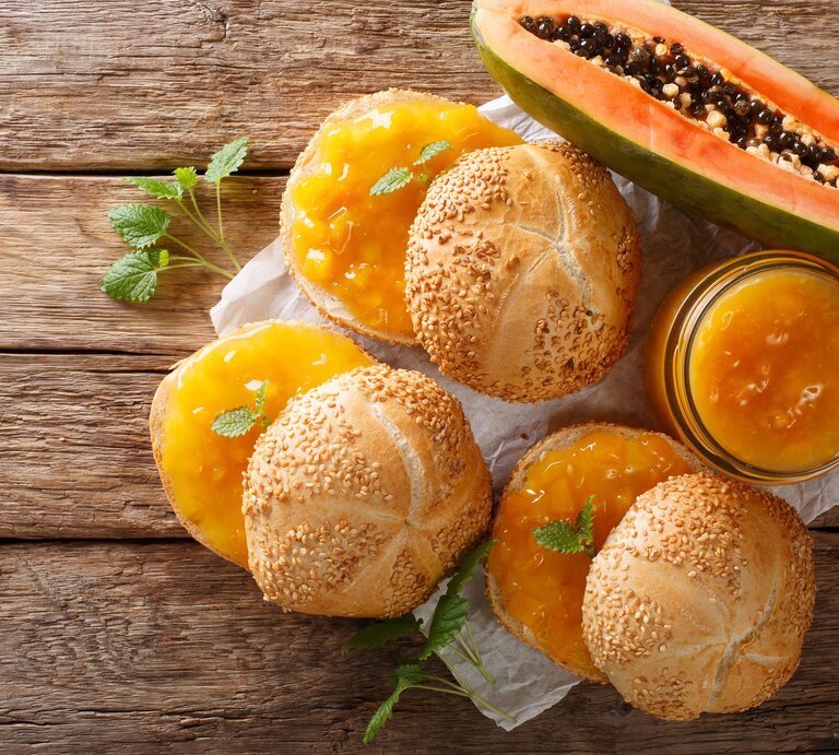 Draufsicht: Drei Brötchen mit einem selbst gemachten Papaya-Aufstrich auf einem Untergrund aus Holz. Daneben liegt eine aufgeschnitten Frucht. | © Shutterstock / AS Foodstudio
