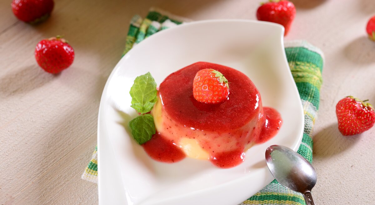 Vanillepaschka mit Erdbeersoße, Erdbeere und Minze in weißer Schale auf grün-weißer Stoffserviette und hellem Holz. Im Bild Erdbeeren als Dekoration. Aufnahme aus der Vogelperspektive.
