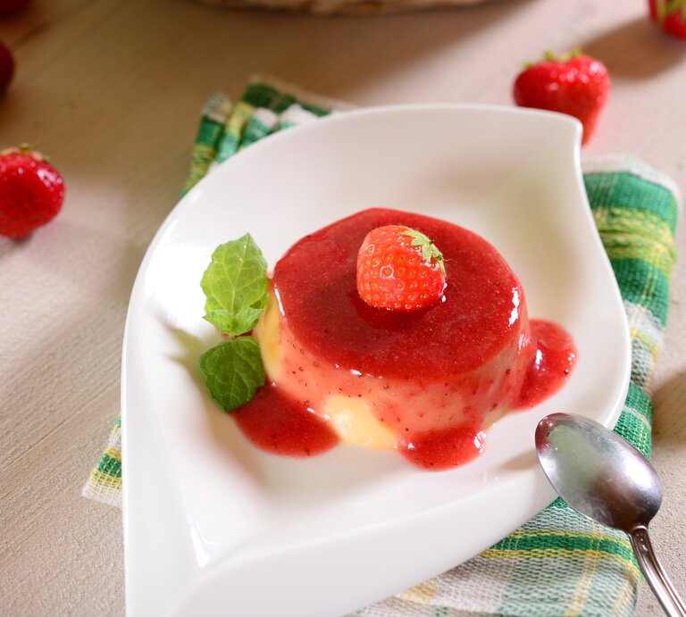Vanillepaschka mit Erdbeersoße, Erdbeere und Minze in weißer Schale auf grün-weißer Stoffserviette und hellem Holz. Im Bild Erdbeeren als Dekoration. Aufnahme aus der Vogelperspektive. | © Shutterstock / Piotr Krzeslak