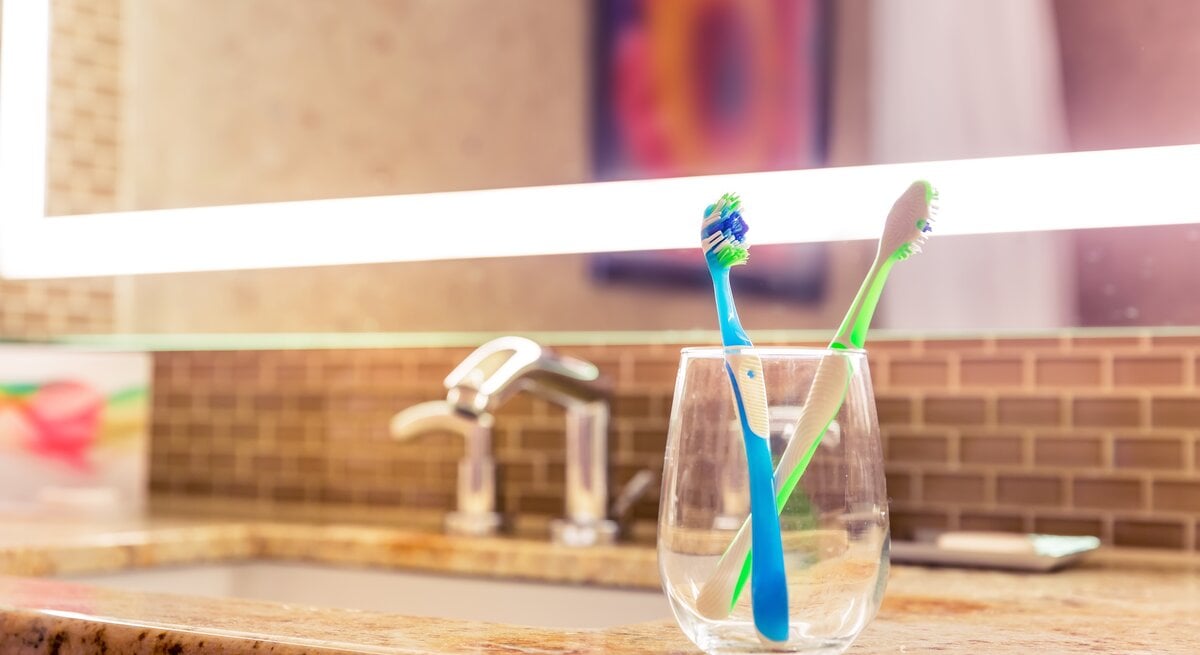 Ein Glas mit zwei Zahnbürsten steht neben dem Waschbecken.