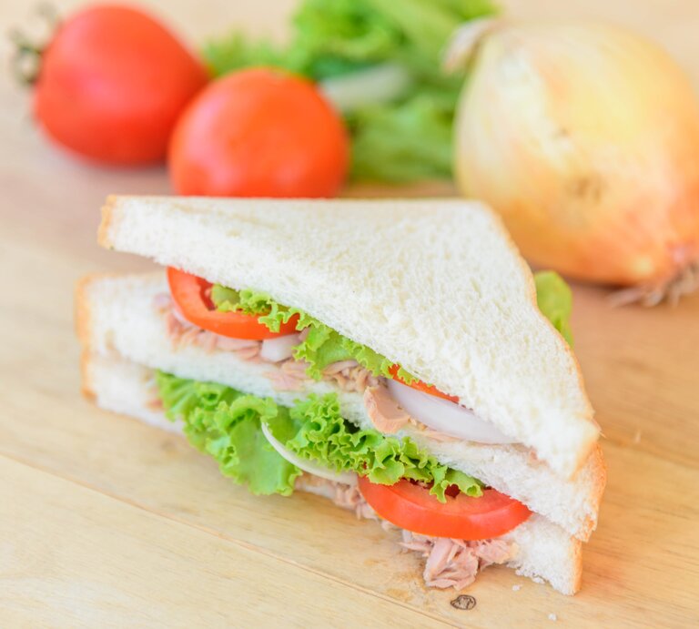 Draufsicht, schräg: Ein Thunfisch-Tramezzini mit Tomate auf einem hellem Untergrund aus Holz. | © Shutterstock / rukawajung