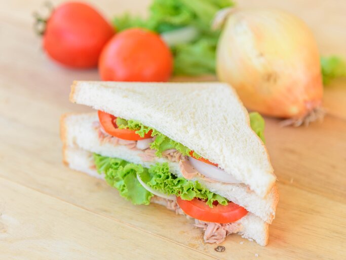Draufsicht, schräg: Ein Thunfisch-Tramezzini mit Tomate auf einem hellem Untergrund aus Holz. | © Shutterstock / rukawajung