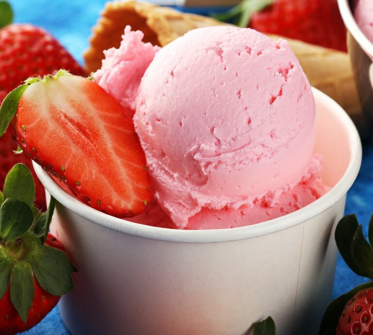 Der Erdbeer-Eisbecher zwischen vielen Erdbeeren und einer Waffel auf einem blauen Tisch. | © Shutterstock/ beats1