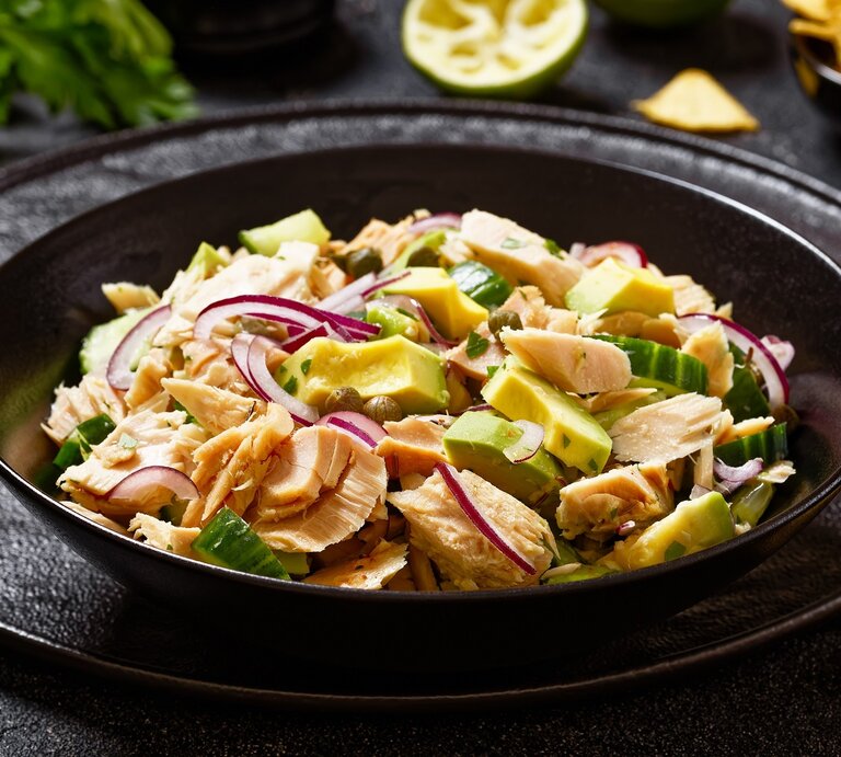 Ein schwarzer Teller mit dem Thunfischsalat, Avocado und Kapern auf einen schwarzen Tisch mit Limette, Nachos und  Petersilie. | © Shutterstock/ from my point of view 