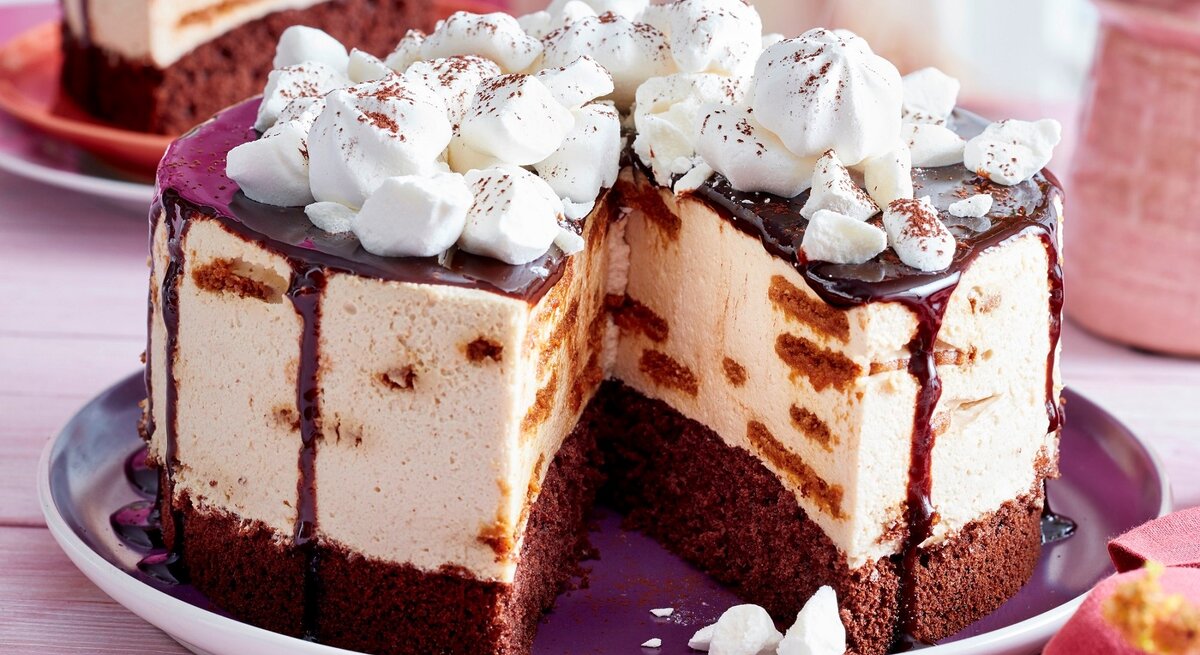 Auf einem Teller liegt eine angeschnittene Schoko-Tiramisu-Torte. Man erkennt die unterschiedlichen Schichten. Sie ist getoppt mit Baisertuffs und Schokoladensoße. 