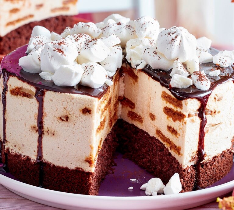 Auf einem Teller liegt eine angeschnittene Schoko-Tiramisu-Torte. Man erkennt die unterschiedlichen Schichten. Sie ist getoppt mit Baisertuffs und Schokoladensoße.  | © EAT CLUB/ Isabell Triemer