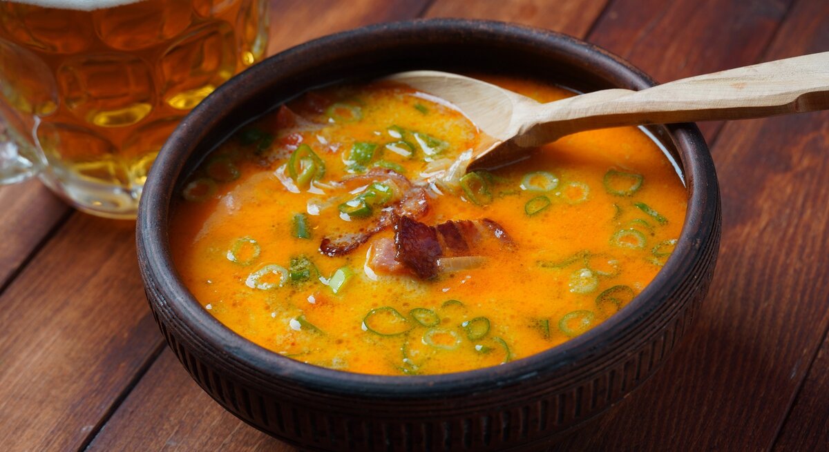 Eine schwarze Schale mit der Cheddar-Bier-Suppe auf einem Holztisch von schräg oben fotografiert.