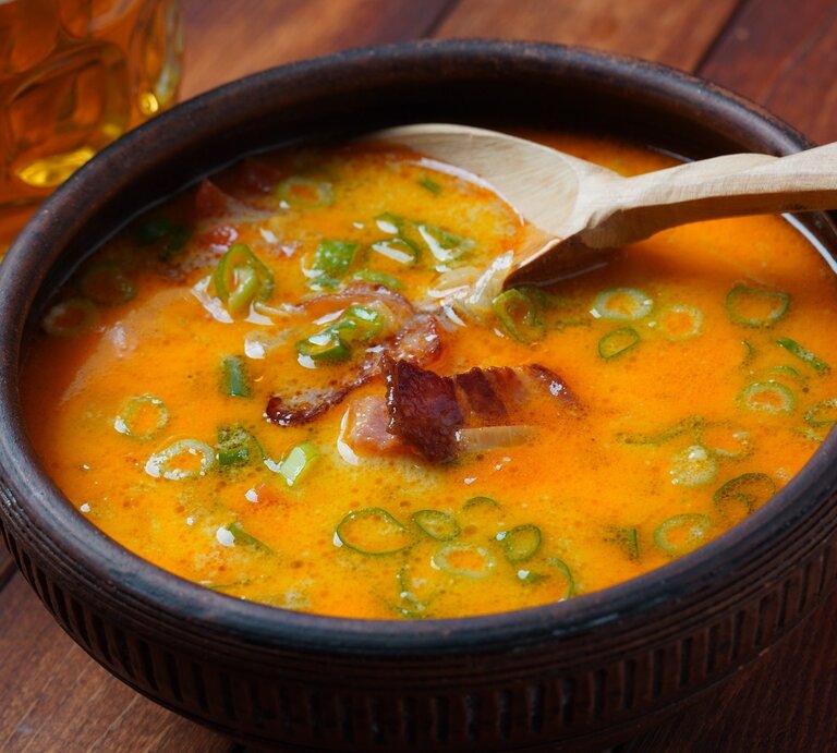 Eine schwarze Schale mit der Cheddar-Bier-Suppe auf einem Holztisch von schräg oben fotografiert. | © Shutterstock/ Natalia Hanin