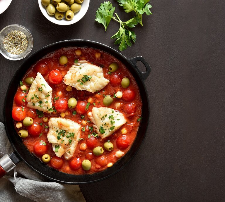 Draufsicht: Eine mediterrane Fischfilet-Pfanne auf dunklem Untergrund. Drum herum liegen Zitronenscheiben, Petersilie und Gewürze. | © Shutterstock / Tatiana Volgutova