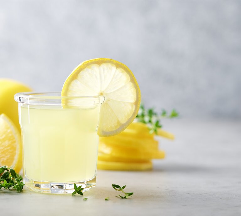 Ein Glas Limoncello Gin Fizz mt einer Zitronenscheibe garniertm, drumherum liegen frische Kräuter und Zitronen, teilweise angeschnitten. | © Adobe Stock/ Anna Puzatykh