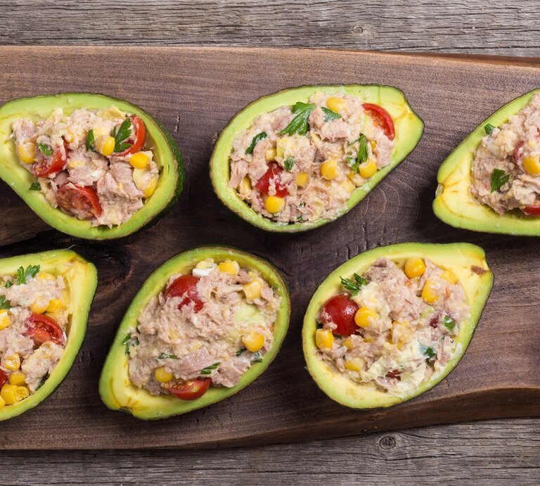 Ein Holzbrett mit sechs Avocadohälften und dem Thunfischsalat. Alles auf einem rustikalem Holztisch direkt von oben fotografiert. | © Shutterstock/ AlexeiLogvinovich 