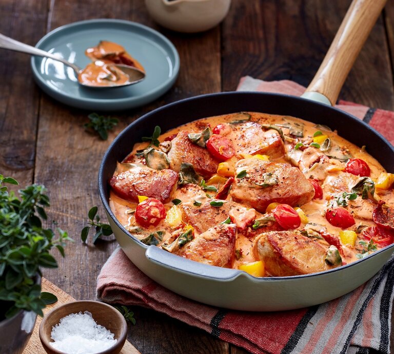 Puten-Tomaten-Pfanne in einer Pfanne auf Küchentuch auf Holzuntergrund. Drum herum Geschirr, ein Schälchen Salz und Kräuter.  | © EAT CLUB / Isabell Triemer