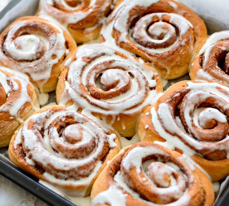 9 Bananen-Zimtschnecken auf einem Blech mit Backpapier, verziert mit Zuckerguss. | © Adobe Stock/ roman