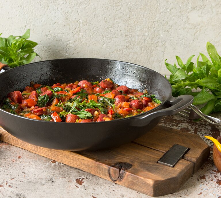 Frontal: Eine Würstchenpfanne mit Kidneys liegt auf einem rustikalen Holzbrett auf einem groben Untergrund. Drum herum liegen Chilis sowie frischer Spinat. | © © Shutterstock / kochabamba