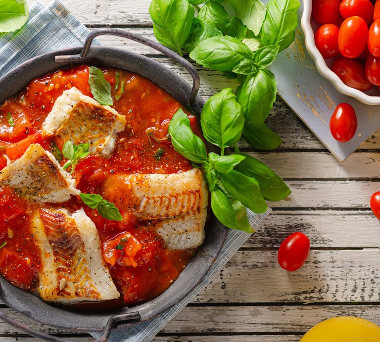 Draufsicht: Holzuntergrund, runder Topf mit geschmorter Seelachs auf mediterranem Gemüse und Tomatensoße. | © Shutterstock / Stepanek Photography