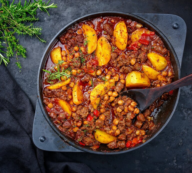 Draufsicht: Eine Hackfleisch-Pfanne mit Kichererbsen auf einem dunklen Untergrund. An der Seite liegen frische Kräuter. | © Shutterstock / hlphoto