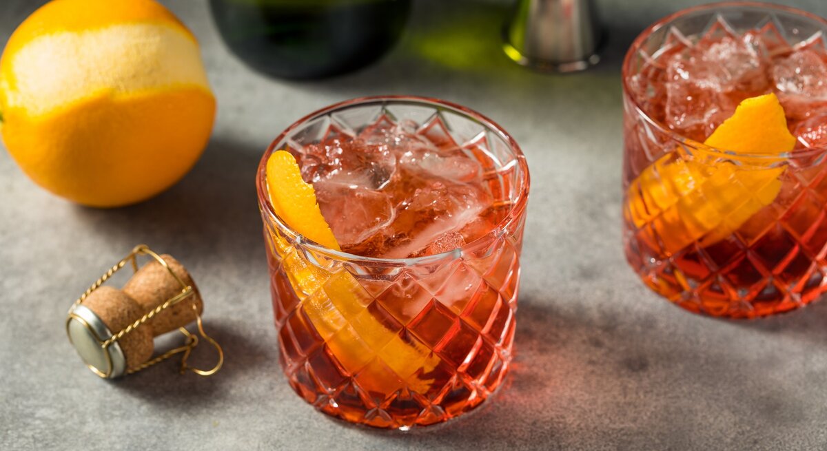 Zwei Gläser mit dem falschen Negroni auf einem Steintisch mit Prosecco und einer Orange.