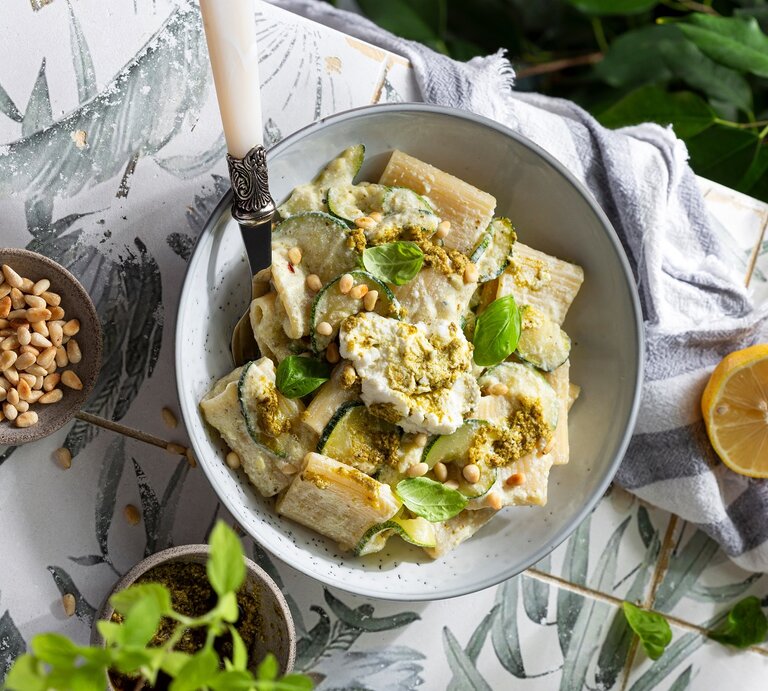 Ein Pastateller mit Nudeln und der Zucchinicreme auf einem Marmortisch mit Zitronen von oben im Sonnenlicht fotografiert. | © Shutterstock/Pronina Marina