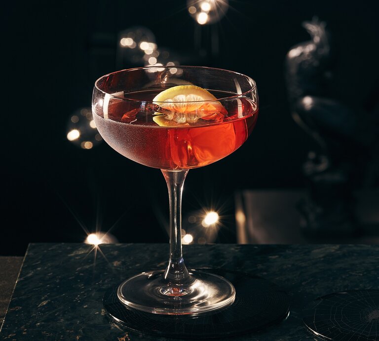 Frontal: Auf einer dunklen Tischplatte steht ein Glas Gin Dubonnet mit EIswürfeln und eine Zitronenschnitzer. | © Getty Images / Image Professionals GmbH