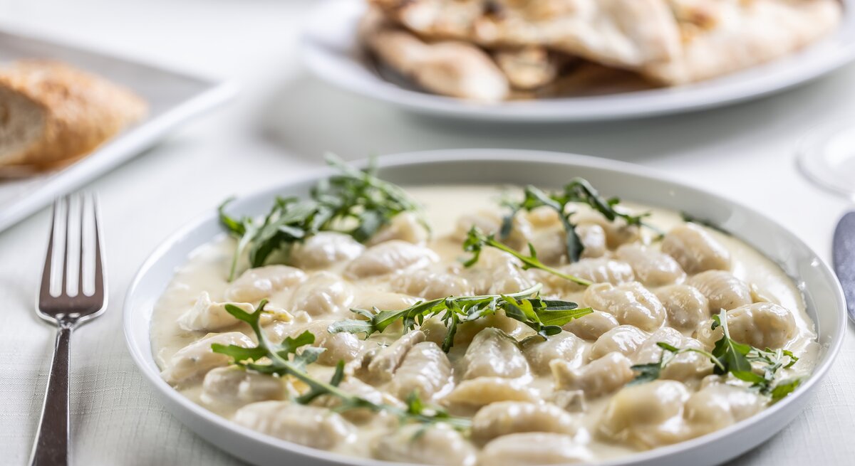 Gnocchi in Vier-Käse-Soße mit Rucola auf weißem Teller. 