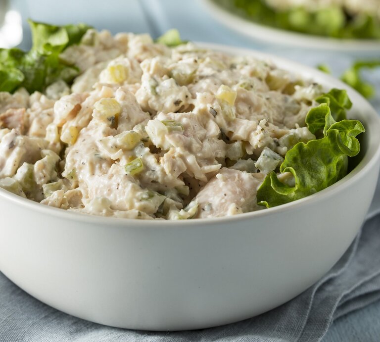 Eine weiße Schüssel mit dem Salat auf einer hellblauen Tischdecke seitlich fotografiert. Im Hintergrund unscharf eine weitere Portion auf dem Teller sowie Salz- und Pfefferstreuer zu erkennen.    | © Shutterstock/ Brent Hofacker