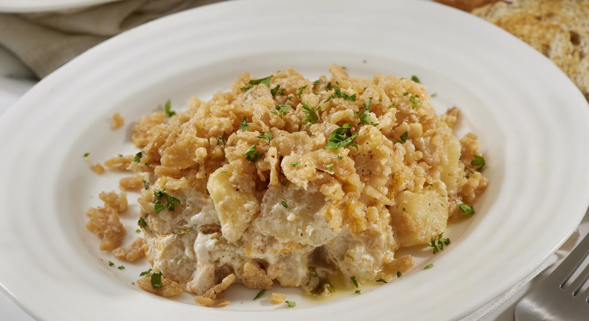 Käsiger Kartoffel-Rösti-Auflauf mit Petersilie bestreut auf einem weißen Teller. 