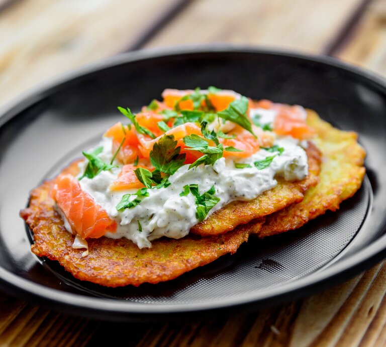 Gebratener Kartoffelpuffer mit Quark und einer Scheibe Räucherlachs belegt.  | © Getty Images/semenovp