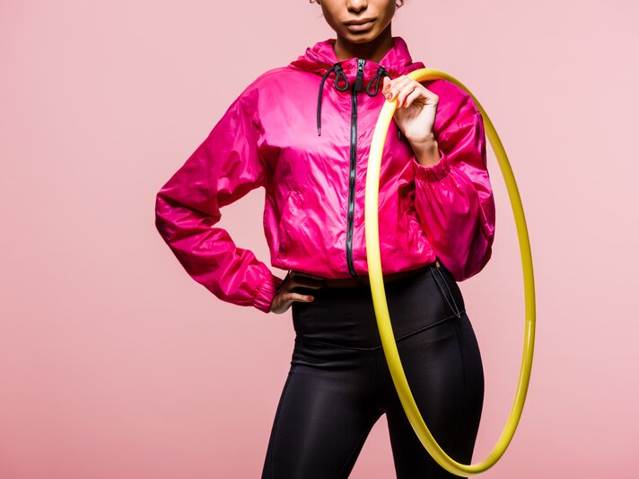 Frau hält Hula-Hoop-Reifen vor einem rosafarbenen Hintergrund | © Adobe Stock/LIGHTFIELD STUDIOS