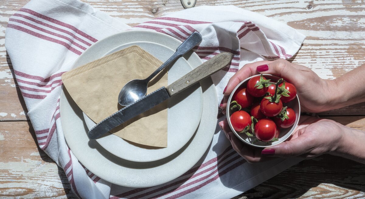 Kaffeefilter sollen zum Polieren von Besteck benutzt werden. Die Papiertüten liegen auf einemTeller. Man sieht Hände einer Frau, die eine Schüssel mit selbst angebauten Tomaten hält.