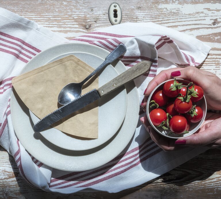 Kaffeefilter sollen zum Polieren von Besteck benutzt werden. Die Papiertüten liegen auf einemTeller. Man sieht Hände einer Frau, die eine Schüssel mit selbst angebauten Tomaten hält. | © GettyImages/Westend61
