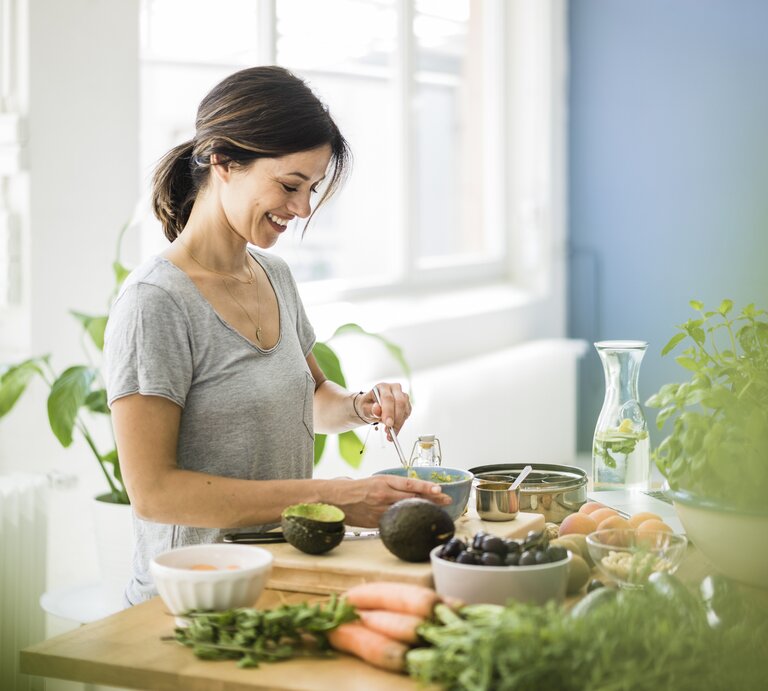 Eine lächelnde Frau bereitet sich ihr veganes Essen zu. | © GettyImages/Westend61