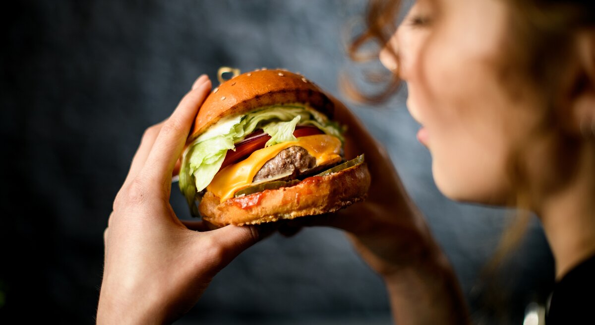 Stiftung Warentest prüft vegetarische und vegane Burger-Pattys: Close-up einer Frau, die einen Burger in den Händen hält. 