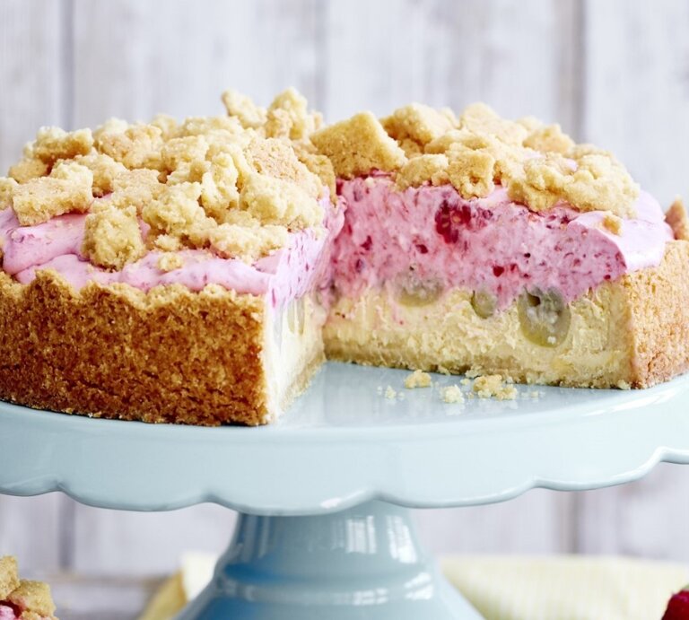 Auf einer Etagerie steht eine Stachelbeer-Quark-Streuseltorte. Sie ist mit einer rosa Creme gefüllt und angeschnitten.  | © EAT CLUB / Isabell Triemer