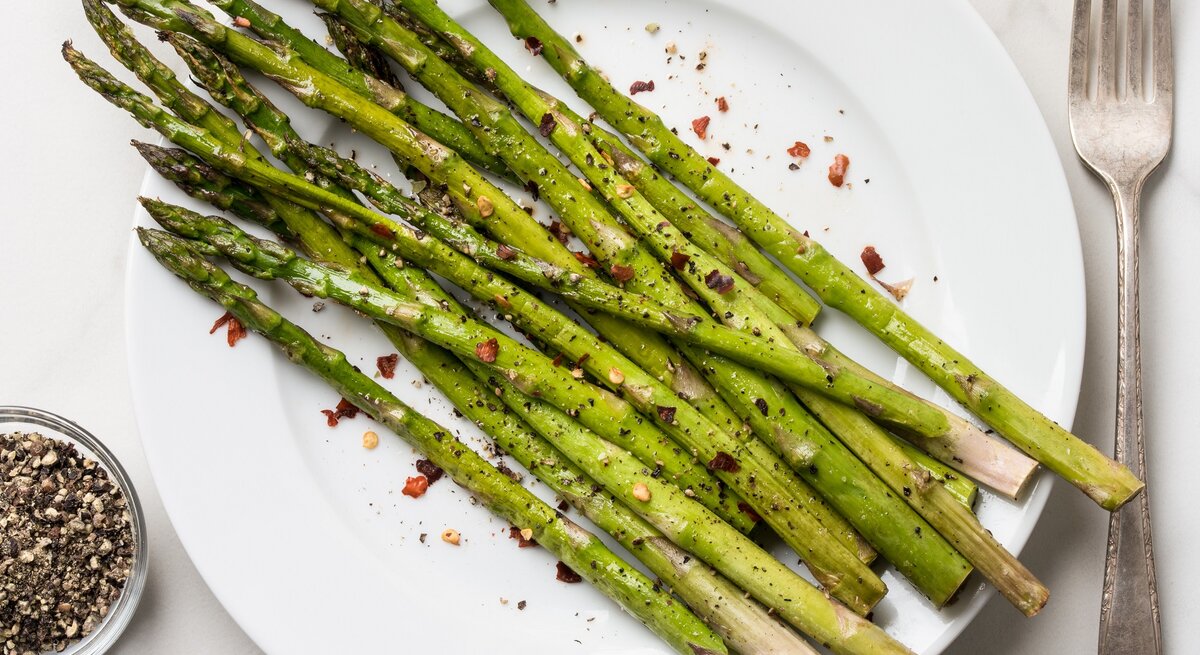 Ein Teller mit Knoblauch-Zitronen-Spargel. daneben eine Gabel, alles Draufsicht.