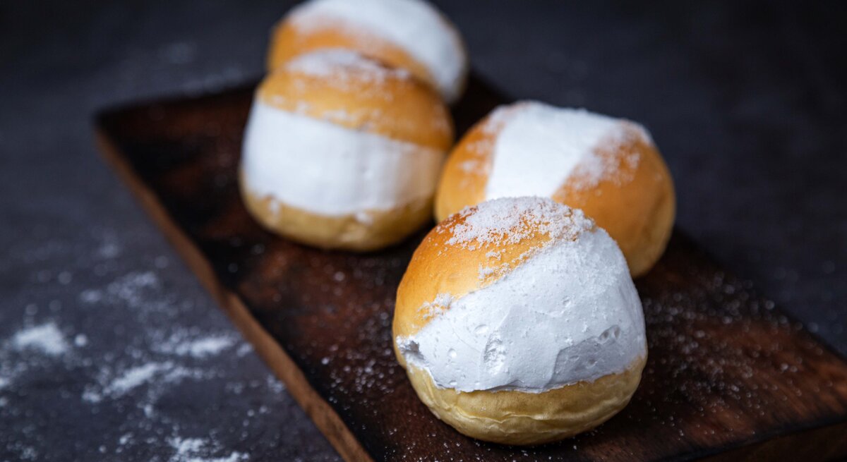 Vier der gefüllten Milchbrötchen auf einem dunklem Holzbrett mit schwarzem Unter- und Hintergrund.