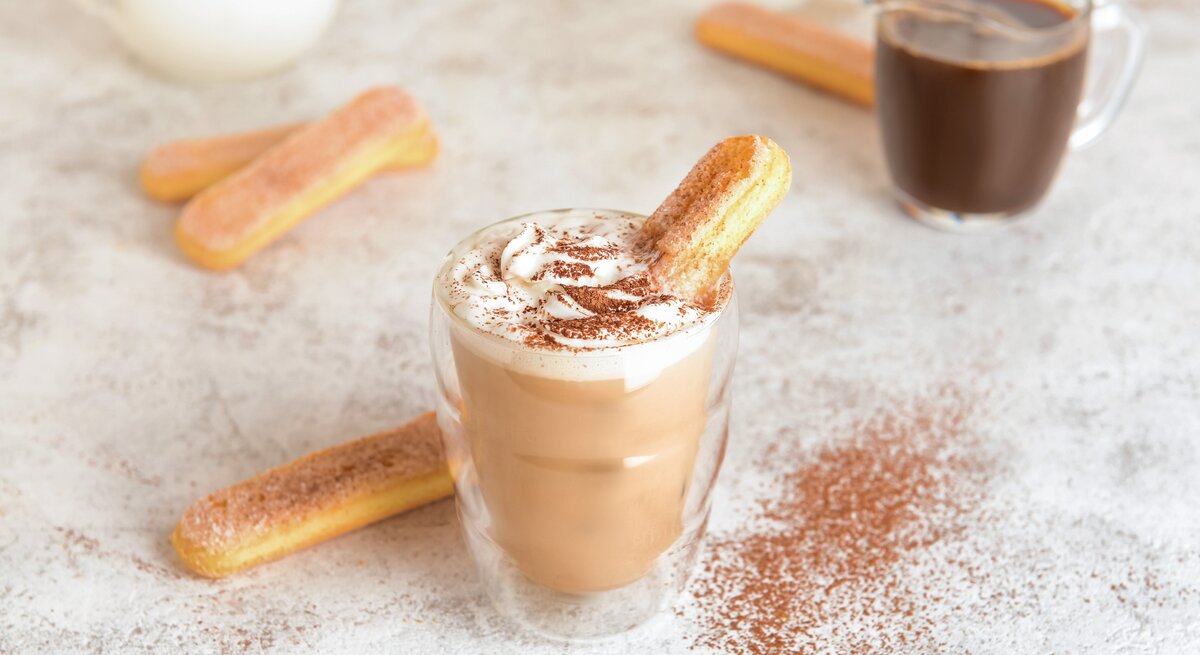 Ein Glas mit Tiramisu-Latte neben einem Löffelbiskuit.
