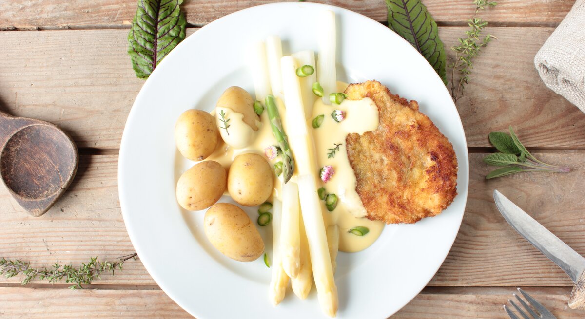  Spargel mit Schnitzel in frühlingshafter Cremesoße mit Kartoffeln auf Holztisch
