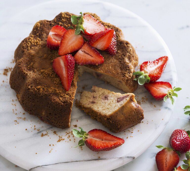 Ein angeschnittener Sauerrahmkuchen mit Erdbeeren auf einem hellen Marmorteller und weißem Untergrund. | © StockFood / Studer, Veronika