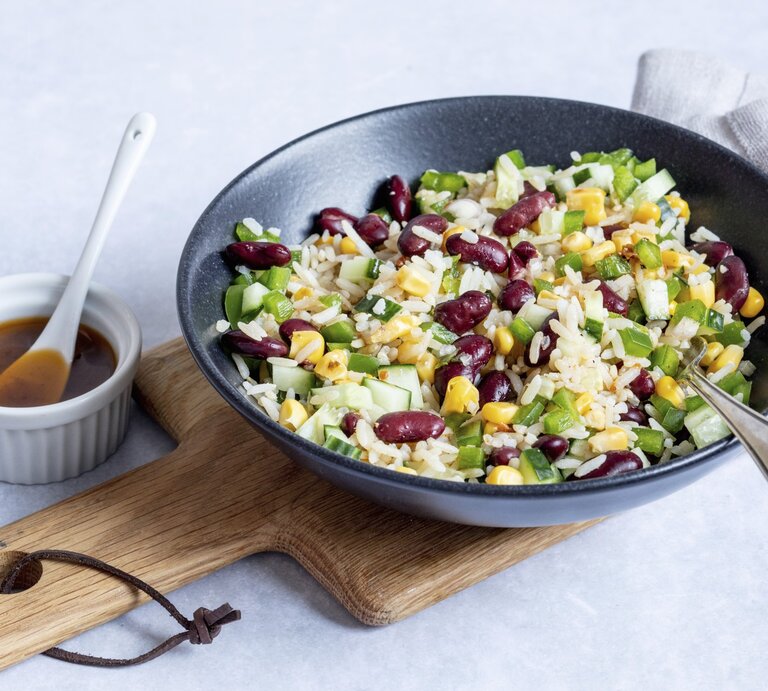 Reissalat mit Mais und Kidneybohnen in einer schwarzen Schüssel. Daneben ein weißes Schälchen mit einem Dressing.  | © StockFood / Timmann, Claudia