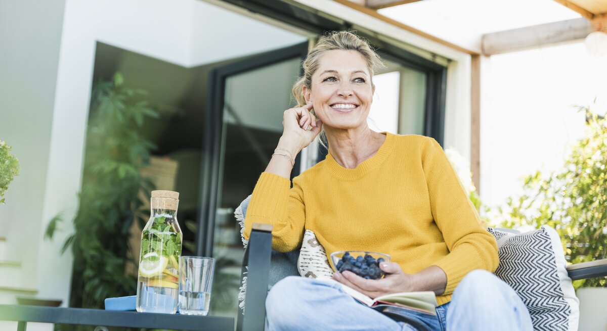 Frau sitzt mit Schale voller Blaubeeren auf einer Terrasse
