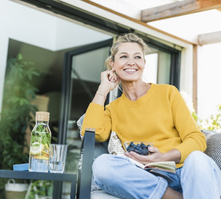Frau sitzt mit Schale voller Blaubeeren auf einer Terrasse | © Getty Imges/Westend61