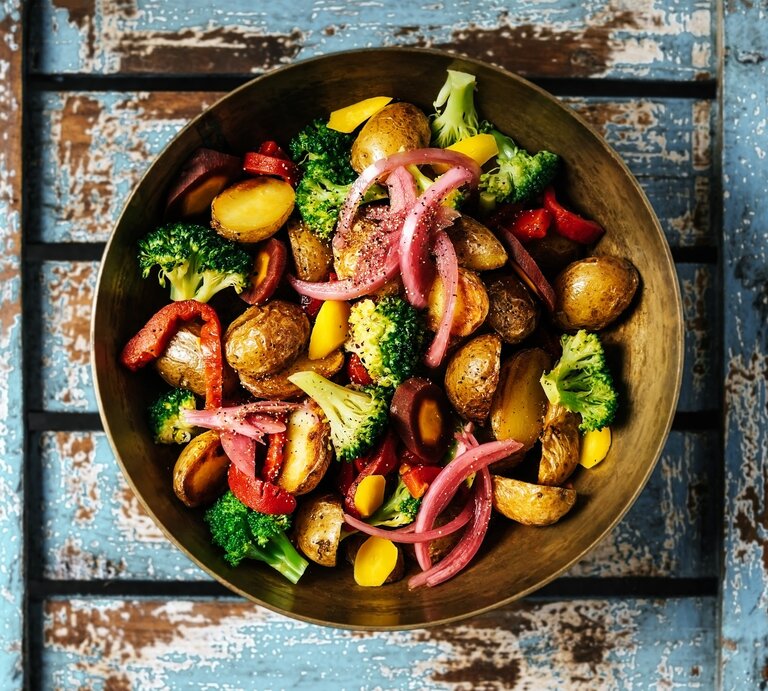 Gegrillter Kartoffelsalat mit Gemüse, Hirtenkäse und rotem Pesto in Schale auf blauem Holz. Aufnahme aus der Vogelperspektive. | © Getty Images / Claudia Totir